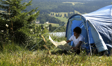 Un jeune adolescent fait du camping et prépare une randonnée en lisant une carte